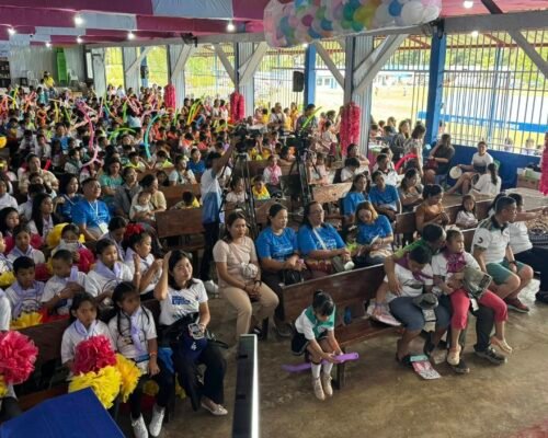 Children sitting in the auditorium, some waving the balloons